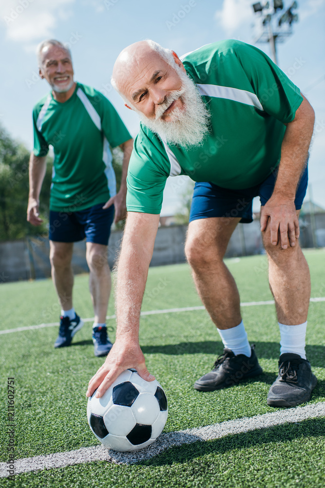 selective focus of elderly beaded men in football uniform with football ball on green field selective focus of elderly beaded men in football uniform with football ball on green field