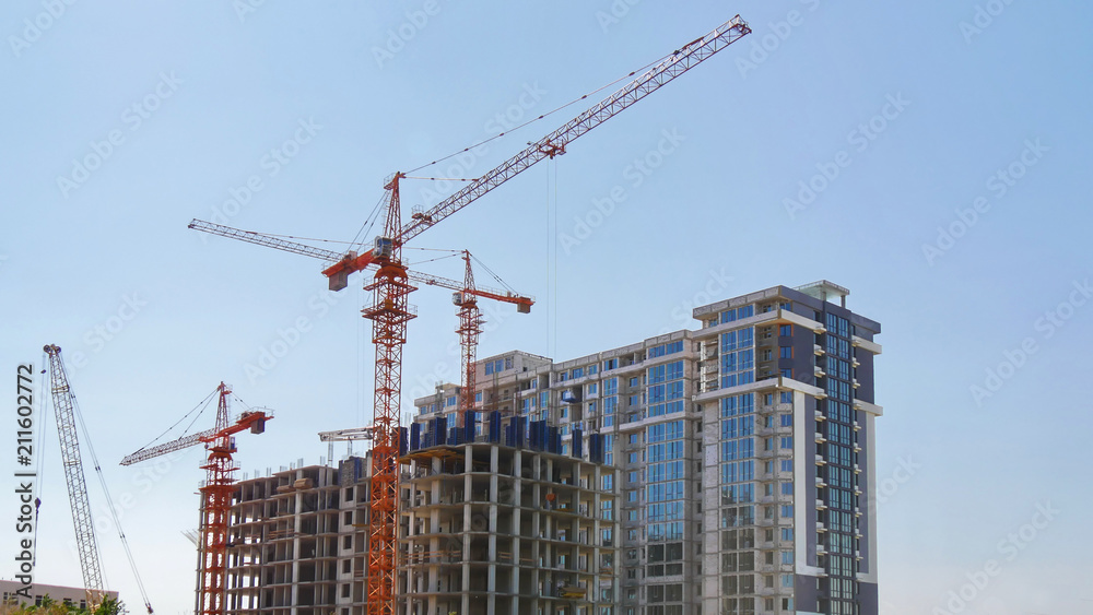 Construction cranes near buildings against blue sky. Construction site.