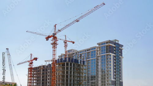 Construction cranes near buildings against blue sky. Construction site.