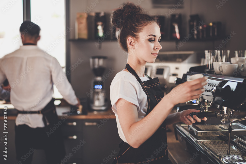 Young woman barista preparing coffee using machine in the cafe