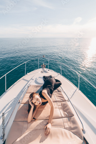 a gorgeous sexy girl in a black summer dress rests on her yacht in the sun, enjoys a vacation