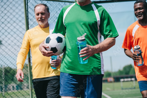 partial view of multicultural elderly men with sportive water bottles and football ball