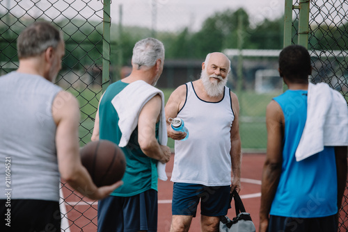 selective focus of group of multiracial old sportsmen with basketball ball on playground