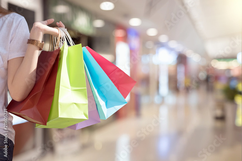 Young woman with shopping bags over shopping mall background - happiness, consumerism, sale season concept