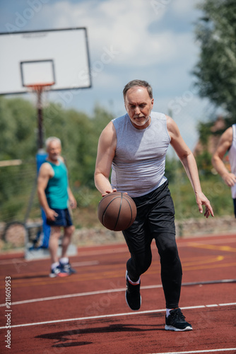 selective focus of old friends playing basketball on summer day