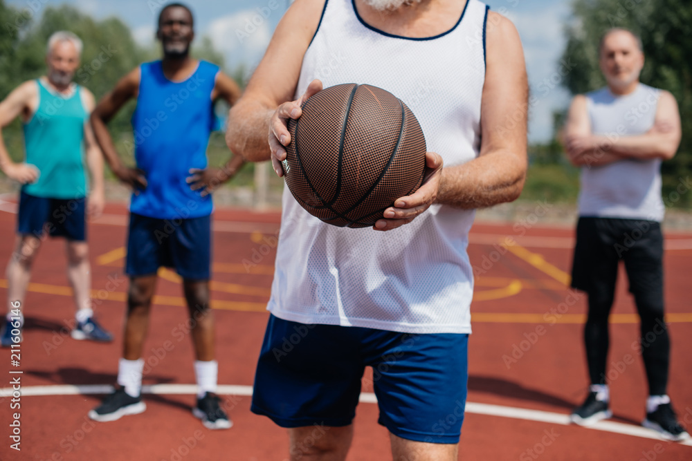 selective focus of multiethnic elderly sportsmen with basketball ball on playground