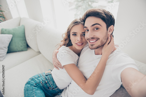 Self portrait of lovely attractive couple shooting selfie on front camera having online meeting sitting on sofa in modern apartments © deagreez