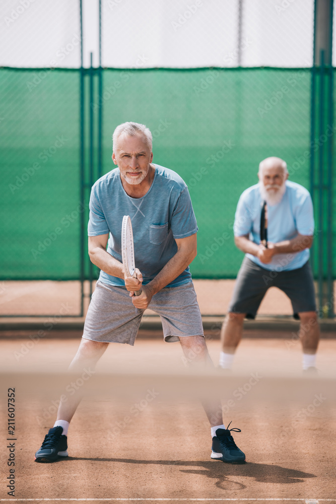 selective focus of elderly men with tennis racquets on court