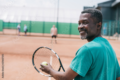 selective focus of smiling elderly african american man playing tennis with friend on court