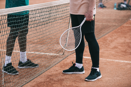 cropped shot of interracial friends with tennis racquet standing near net © LIGHTFIELD STUDIOS