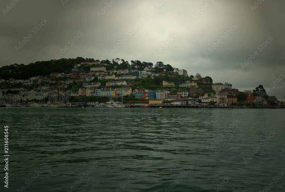 A  view from the river Dart of the town of Kingswear on a summers days with a threatening storm from two directions. Yachts are moored close into the marina in anticipation.