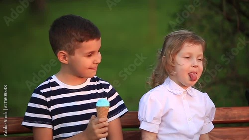 Boy eating an ice cream and sitting on the bench while girl is looking
