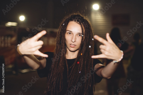 Portrait of a beautiful punk girl with dreadlocks showing a horn symbol at a rock concert. Hipster Nightlife
