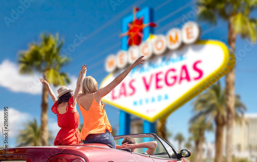 summer holidays, road trip and travel concept - happy friends driving in convertible car and waving hands over welcome to fabulous las vegas sign background