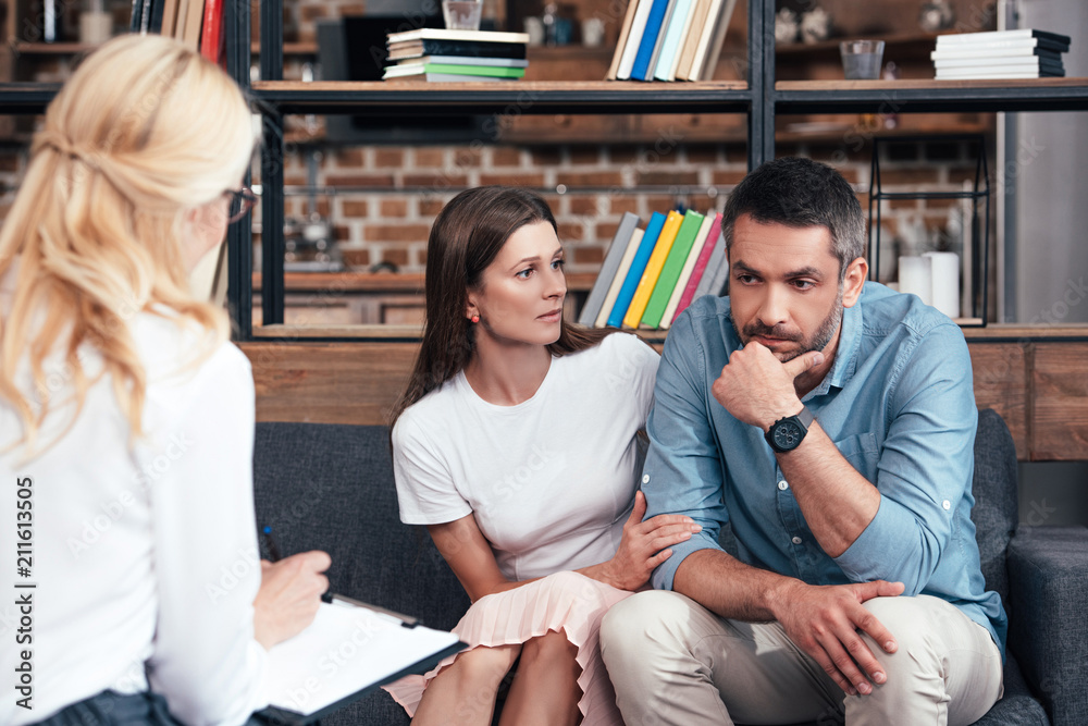 woman embracing stressed husband on therapy session by female counselor in office woman embracing stressed husband on therapy session by female counselor in office