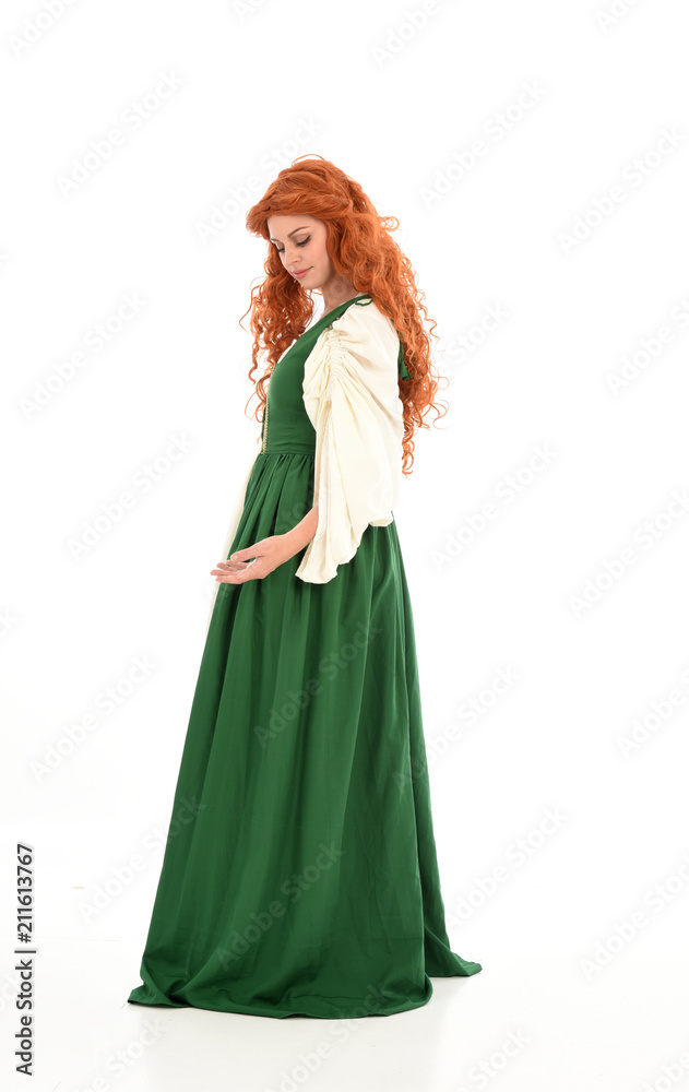 full length portrait of red haired girl wearing long green gown,. standing pose with back to the camera, isolated on white studio background.