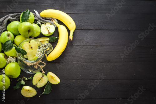 A glass jar of fresh water with apples and bananas on the black wooden background. Copy space. Healthy food, detox