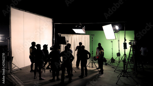 Behind the scenes of TV commercial movie film or video shooting production which crew team and camera man setting up green screen for chroma key technique in big studio.