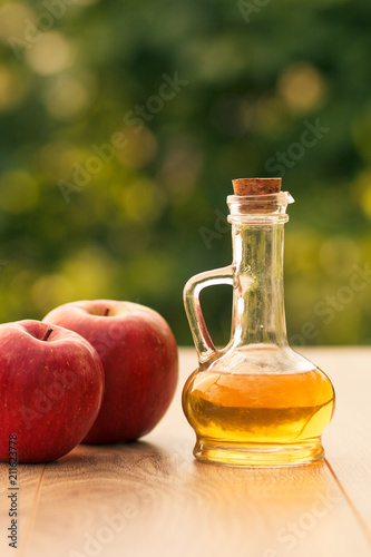 Apple cider vinegar in glass bottle and fresh red apple on wooden boards with green natural background