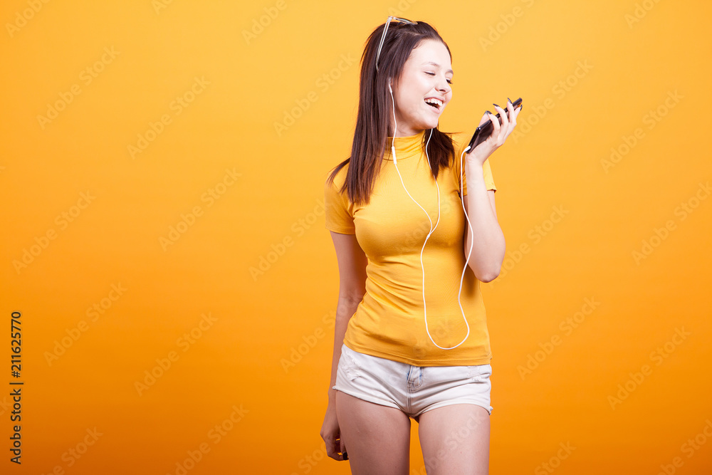 Cute young woman singing on her phone while dancing in studio on yellow background Cute young woman singing on her phone while dancing in studio on yellow background