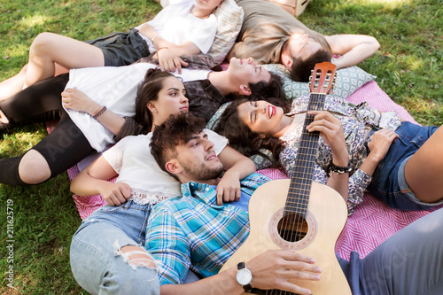 friendship, leisure and summer concept - group of happy smiling friends with guitar chilling on picnic blanket