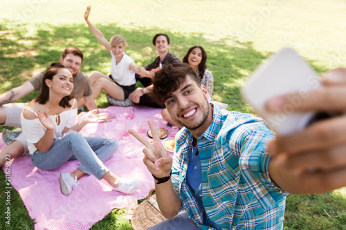 friendship  leisure and technology concept - group of happy smiling friends taking selfie by smartphone chilling on picnic blanket at summer park