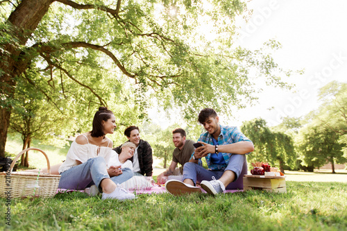 friendship, leisure, technology and people concept - group of friends with smartphones chilling on picnic blanket at summer park