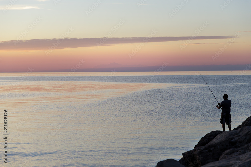 Silhouette of man with fishing spinning. Fishing on the lake at beautiful sunset. Lake Ontario. Rochester, USA