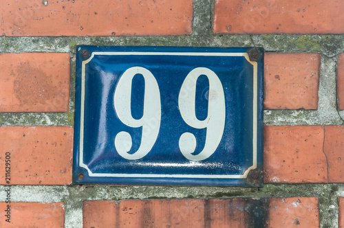 Old vintage house address blue metal number 99 ninety nine on the brick facade of residential building exterior wall on the street side