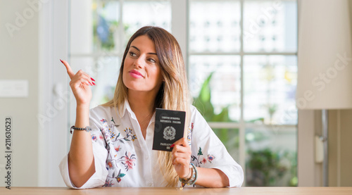 Young woman at home holding a passport of Italy very happy pointing with hand and finger to the side