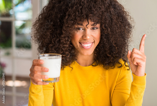 African american woman holding a glass of milk surprised with an idea or question pointing finger with happy face, number one