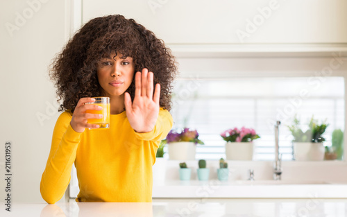 Schilderij op canvas African american woman drinking orange juice in a glass with open hand doing sto
