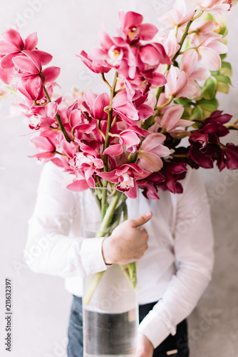 Fototapeta Naklejka Na Ścianę i Meble -  Very nice young man in a white shirt holding a huge bunch of Cymbidium orchid flowers, covering his face 