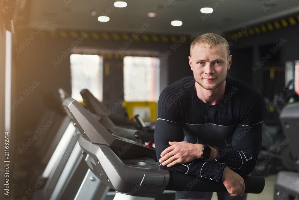 Young man having rest in gym after running on treadmill