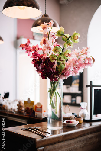 A huge bunch of Cymbidium Orchids in a transparent glass vase standing on a bar counter, decorating room interior