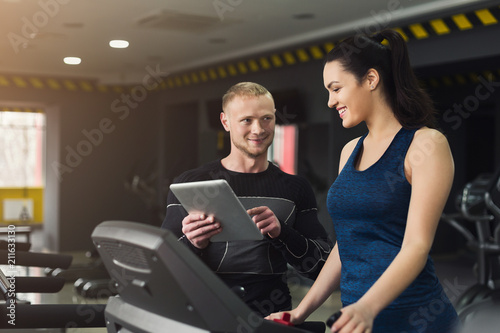 Fitness coach helps woman on elliptical trainer © Prostock-studio