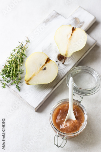 Pear jam, fresh pears and thyme on wooden board on light background.