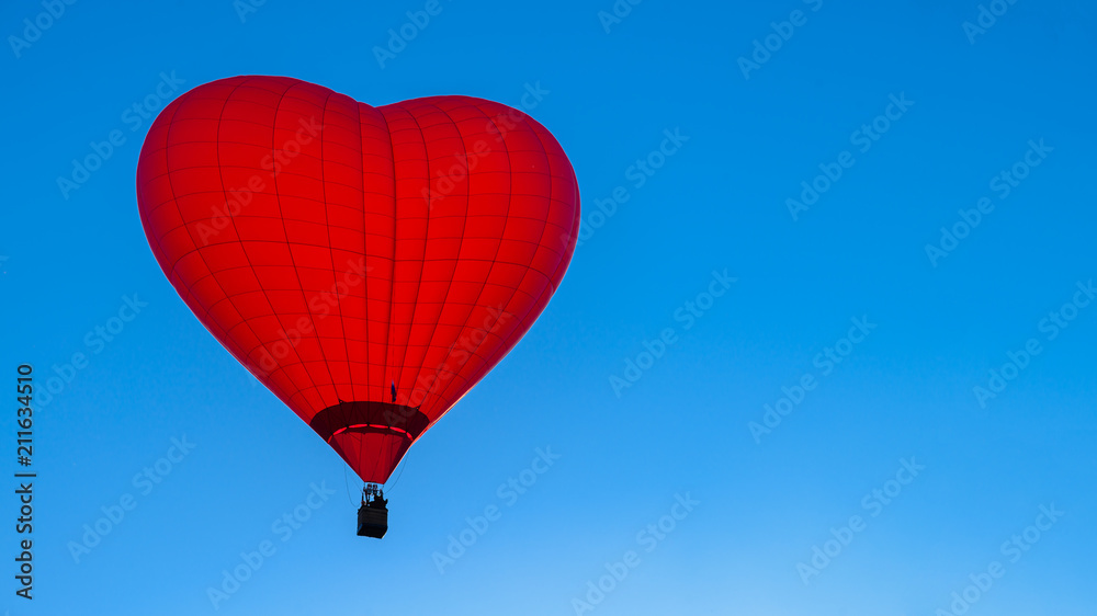 Fototapeta premium Bright red hot air balloon in the shape of heart against blue sk