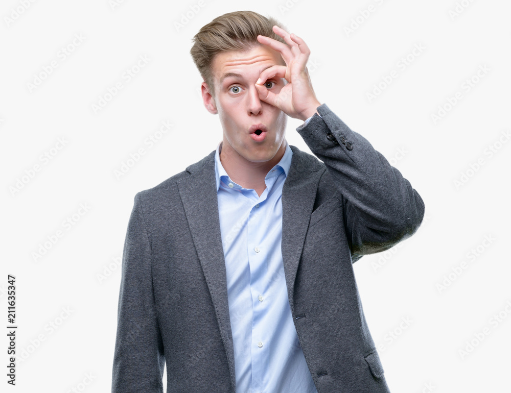 Young handsome blond business man doing ok gesture shocked with surprised face, eye looking through fingers. Unbelieving expression. Young handsome blond business man doing ok gesture shocked with surprised face, eye looking through fingers. Unbelieving expression.