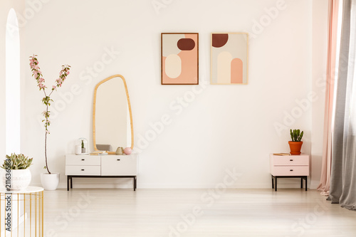 Mirror on white cabinet and plant in bright dressing room interior with posters and copy space. Real photo photo