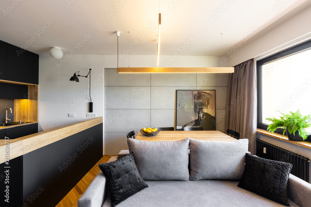 Pillows on grey sofa in modern apartment interior with black kitchen and  light above table. Real photo Stock Photo | Adobe Stock