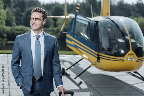 Successful trip. Handsome young businessman smiling contentedly and carrying his suitcase while leaving a helipad having completed a successful trip