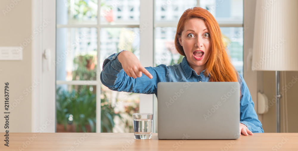 Redhead woman using computer laptop at home very happy pointing with hand and finger Redhead woman using computer laptop at home very happy pointing with hand and finger