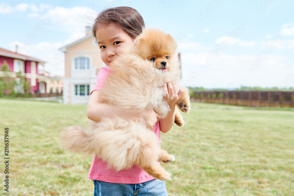 Waist up portrait of cute Asian girl posing with Pomeranian puppy standing in front yard of two storey house, copy space Waist up portrait of cute Asian girl posing with Pomeranian puppy standing in front yard of two storey house, copy space
