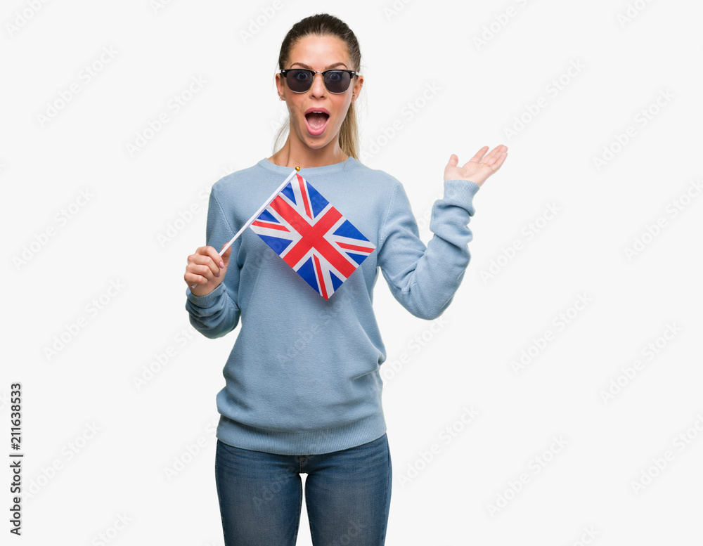 Beautiful young woman holding UK flag very happy and excited, winner expression celebrating victory screaming with big smile and raised hands Beautiful young woman holding UK flag very happy and excited, winner expression celebrating victory screaming with big smile and raised hands