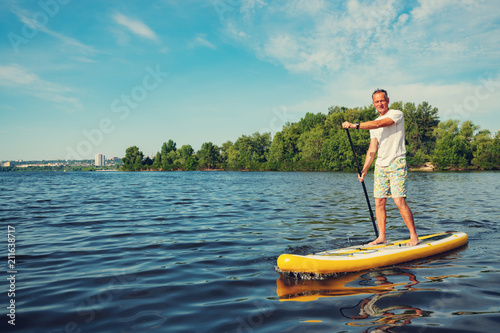 Joyful man is training SUP board in large river