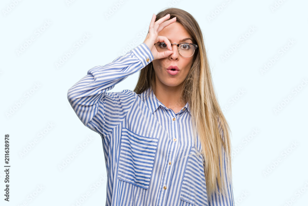 Beautiful young woman wearing elegant shirt and glasses doing ok gesture shocked with surprised face, eye looking through fingers. Unbelieving expression. Beautiful young woman wearing elegant shirt and glasses doing ok gesture shocked with surprised face, eye looking through fingers. Unbelieving expression.