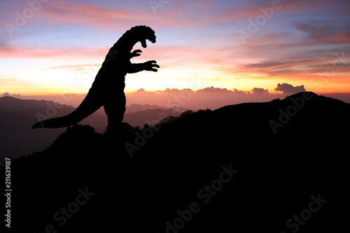 Silhouette eines Godzilla-artigen Monsters auf einem Berg bei Sonnenaufgang