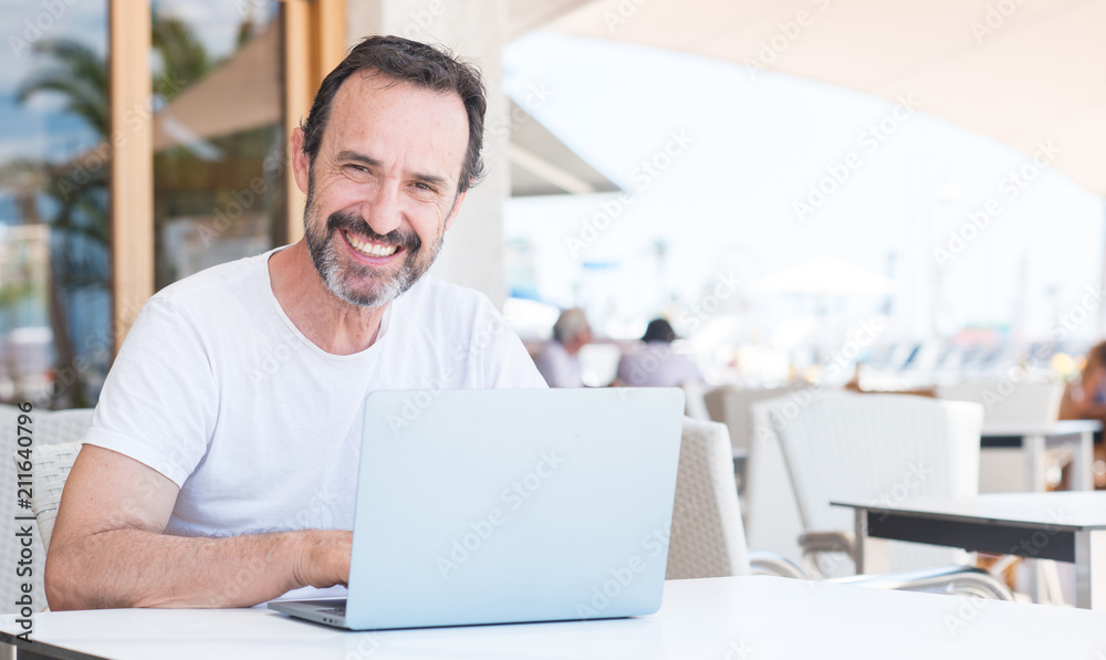 Handsome senior man using laptop at restaurant with a happy face standing and smiling with a confident smile showing teeth Handsome senior man using laptop at restaurant with a happy face standing and smiling with a confident smile showing teeth