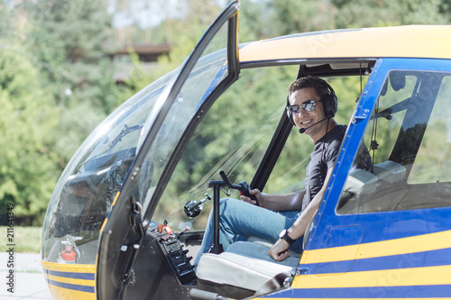 Pilot training. Upbeat young man sitting in a pilot booth of a helicopter and smiling at the camera, being ready to start his training